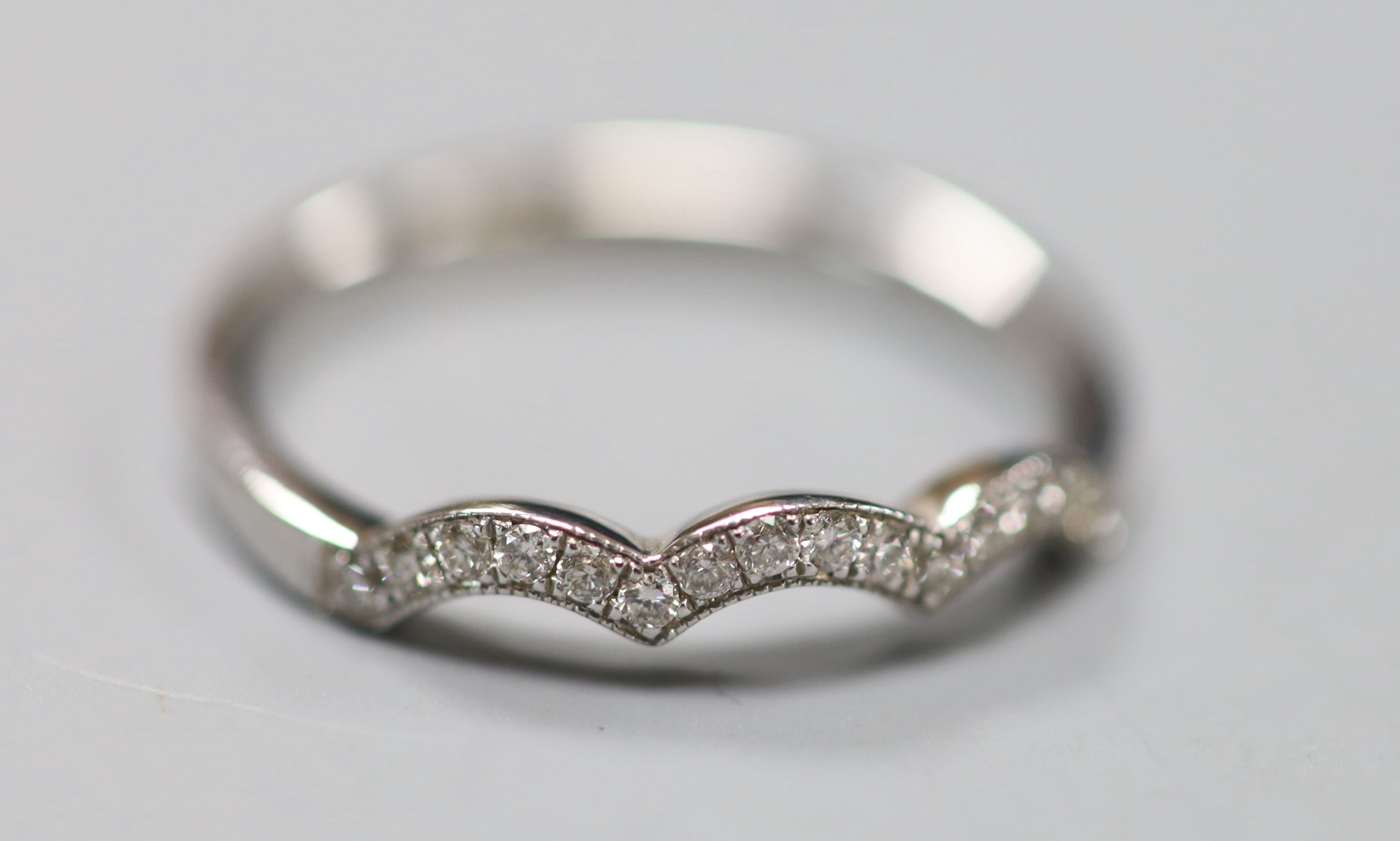 A modern white metal (stamped 14kt) and diamond chip set scallop edge half eternity ring, size O, gross 2.3 grams.